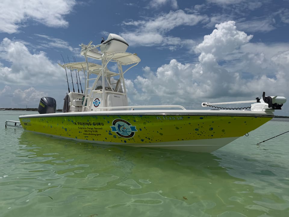 The A Fishing Guru charter boat with a bright yellow hull and logo, moored in shallow crystal-clear Florida Keys water