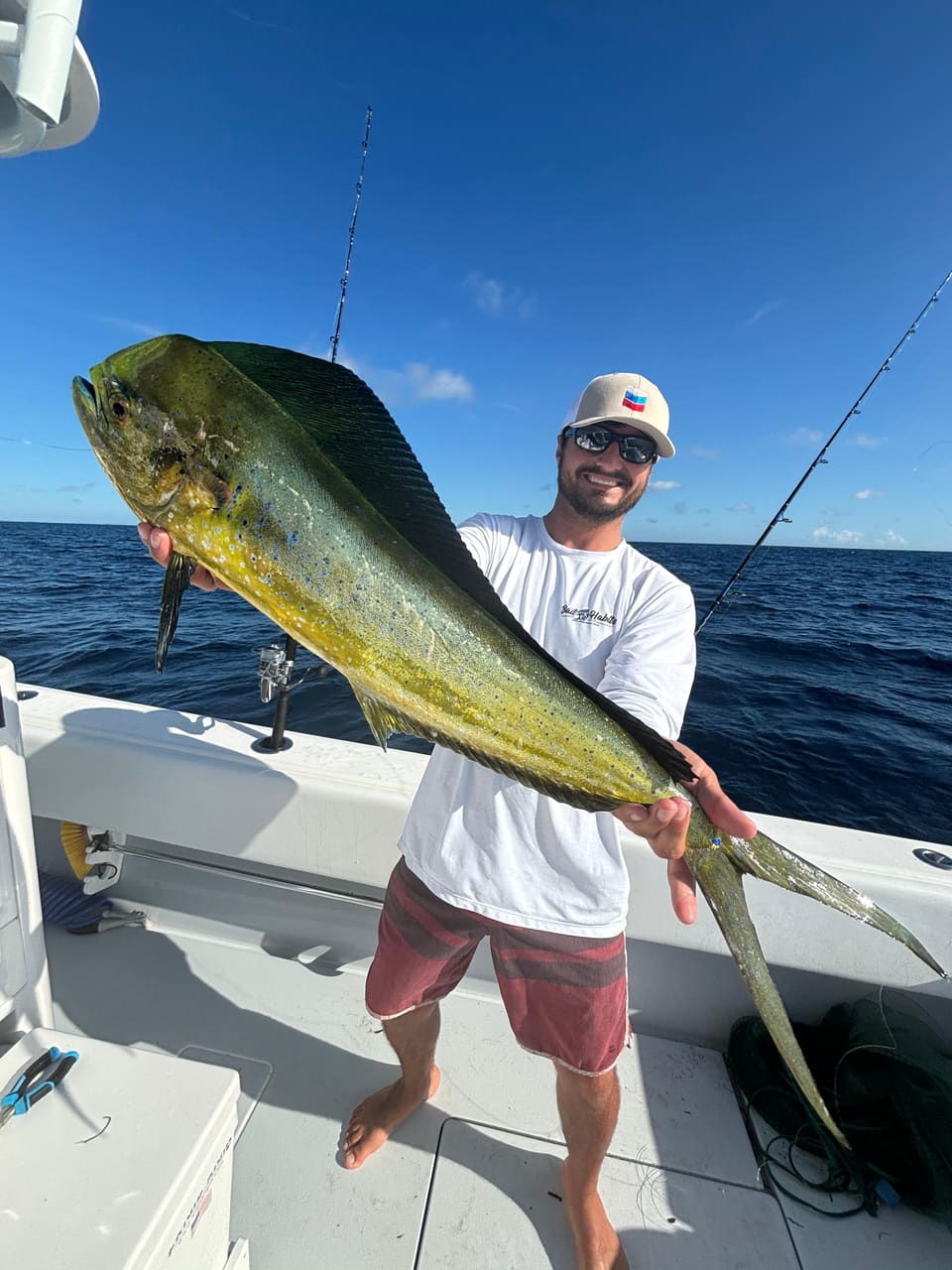 Angler holding a large mahi-mahi (bull dolphin) with vivid green and yellow coloring on a charter boat in the open ocean under a blue sky