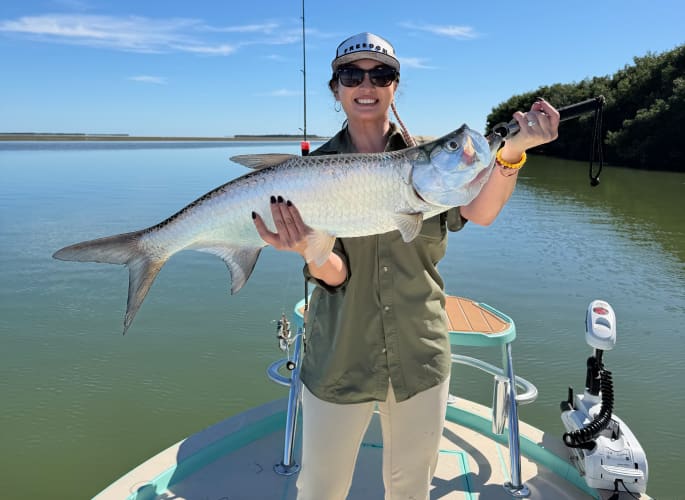 A woman happily holds up a large silver game fish caught while inshore fishing 
